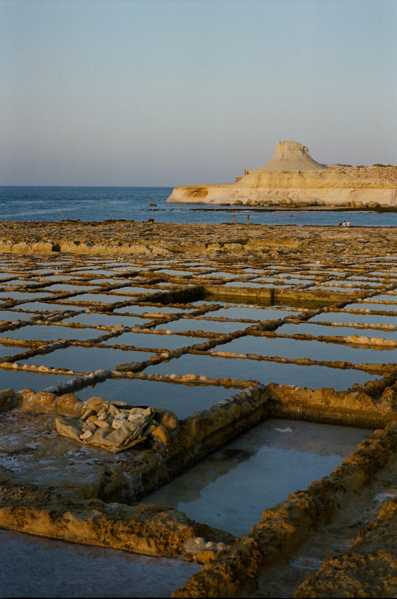 Salt pans by the ocean with distant rocky hills.